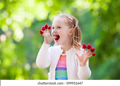 Child Picking Raspberry. Kids Pick Fresh Fruit On Organic Raspberries Farm. Children Gardening And Harvesting Berry. Toddler Kid Eating Ripe Healthy Berries. Outdoor Family Summer Fun In The Country