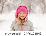 A child in a pink hat plays with a colorful toy in the snow in front of a house, enjoying a winter day.