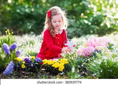 Child Planting Spring Flowers In Sunny Garden. Little Girl Gardener Plants Hyacinth, Daffodil, Snowdrop In Flower Bed. Gardening Tools And Water Can For Kids. Family With Children Work In The Backyard