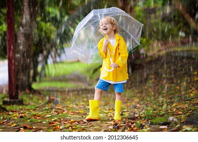 Child Playing In Autumn Rain. Kid With Umbrella. Little Boy Running In A Park In Fall Season. Outdoor Fun For Kids By Any Weather. Rain Waterproof Wear, Boots And Jacket For Children.