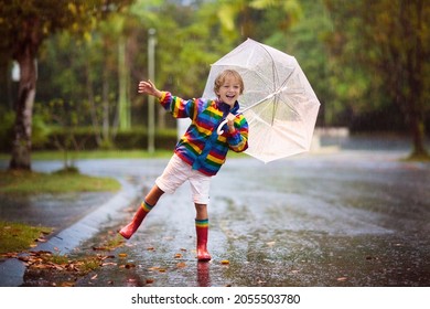 Child Playing In Autumn Rain. Kid With Umbrella. Little Boy Running On City Street In Fall Season. Outdoor Fun For Kids By Any Weather. Rain Waterproof Wear, Boots And Jacket For Children.