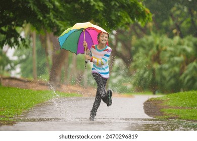 Child playing in autumn rain. Kid jumping in muddy puddle in beautiful park. Little boy with colorful umbrella under heavy fall shower. Stormy rainy weather fun. - Powered by Shutterstock