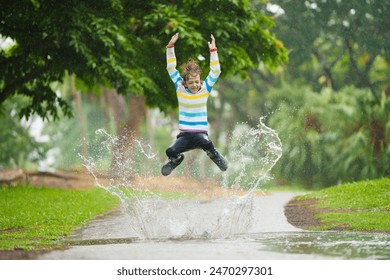 Child playing in autumn rain. Kid jumping in muddy puddle in beautiful park. Little boy with colorful umbrella under heavy fall shower. Stormy rainy weather fun. - Powered by Shutterstock