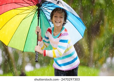 Child playing in autumn rain. Kid jumping in muddy puddle in beautiful park. Little boy with colorful umbrella under heavy fall shower. Stormy rainy weather fun. - Powered by Shutterstock