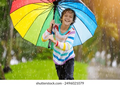 Child playing in autumn rain. Kid jumping in muddy puddle in beautiful park. Little boy with colorful umbrella under heavy fall shower. Stormy rainy weather fun. - Powered by Shutterstock