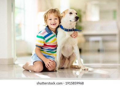 Child Playing With Baby Dog. Kids Play With Puppy. Little Boy And Large Dog At Home. Children And Friendship. Kid Sitting On The Floor With Pet. Animal Care.