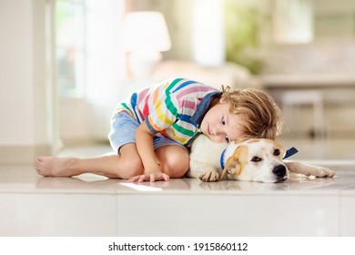 Child Playing With Baby Dog. Kids Play With Puppy. Little Boy And Large Dog At Home. Children And Friendship. Kid Sitting On The Floor With Pet. Animal Care.