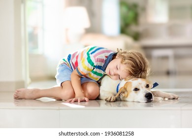 Child Playing With Baby Dog. Kids Play With Puppy. Little Boy And Large Dog At Home. Children And Friendship. Kid Sitting On The Floor With Pet. Animal Care.