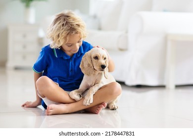 Child Playing With Baby Dog. Kids Play With Puppy. Little Boy And American Cocker Spaniel At Couch At Home. Children And Pets At Home. Kid Sitting On The Floor With Pet. Animal Care.