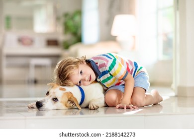 Child Playing With Baby Dog. Kids Play With Puppy. Little Boy And Large Dog At Home. Children And Friendship. Kid Sitting On The Floor With Pet. Animal Care.