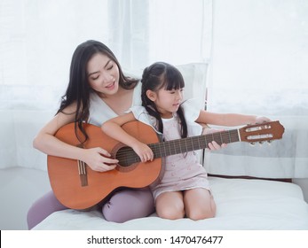 The Child Is Playing In Bed With Her Mother,
Mom Is Singing With Her Daughter And Playing Guitar