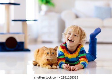 Child playing with cat at home. Kids and pets. Little boy feeding and petting cute ginger color cat. Cats tree and scratcher in living room interior. Children play and feed kitten. Home animals. - Shutterstock ID 2181188313