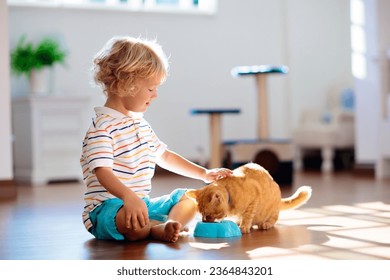 Child playing with cat at home. Kids and pets. Little boy feeding and petting cute ginger color cat. Cats tree and scratcher in living room interior. Children play and feed kitten. Home animals. - Powered by Shutterstock