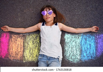 A child playing with chalk drawing rainbow. Child playing and pretending to fly.  Rainbow pride person.