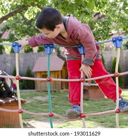 Child Playing At Children Playground, Climbing On  Rope Ladder Obstacle Course Equipment.