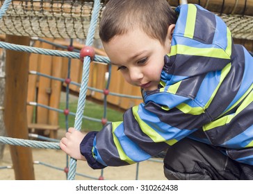 Child Playing At Children Playground, Climbing The  Rope Ladder Frame.