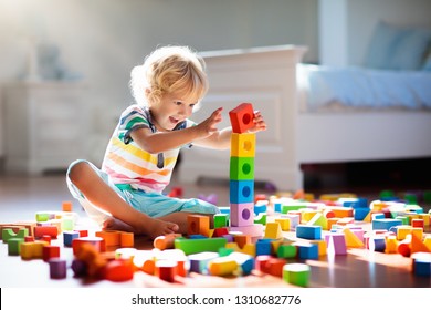 Child Playing With Colorful Toy Blocks. Kids Play. Little Boy Building Tower Of Block Toys Sitting On Dark Floor In Sunny White Bedroom. Educational Game For Baby And Toddler. Children Build Toy House