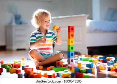 Child playing with colorful toy blocks. Kids play. Little boy building tower of block toys sitting on dark floor in sunny white bedroom. Educational game for baby and toddler. Children build toy house
