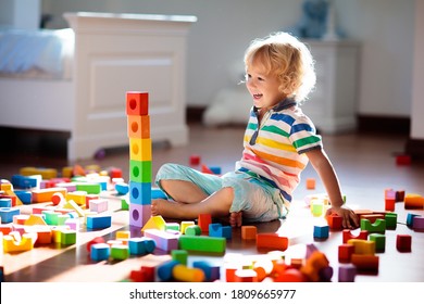 Child Playing With Colorful Toy Blocks. Kids Play. Little Boy Building Tower Of Block Toys Sitting On Dark Floor In Sunny White Bedroom. Educational Game For Baby And Toddler. Children Build Toy House