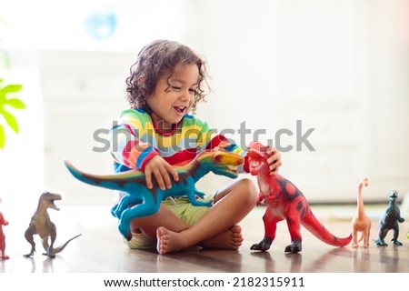 Child playing with colorful toy dinosaurs. Educational toys for kids. Little boy learning fossils and reptiles. Children play with dinosaur toys. Evolution and paleontology game for young kid.