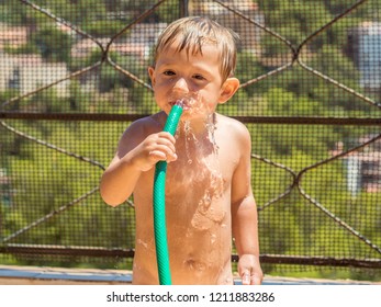 Child Playing And Cooling Off From The Heat With Water And With A Hose