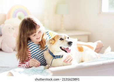 Child Playing With Dog. Girl And Large Dog Relaxing On White Bed At Home. Children And Friendship. Kids Play With Puppy. Kid Hugging Pet. Animal Care. Sunny Morning, Family Time.