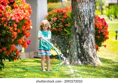 Child playing in garden, pours from the hose, makes a rain. Happy childhood concept.