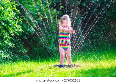 Child Playing With Garden Sprinkler. Kid In Bathing Suit Running And Jumping. Kids Gardening. Summer Outdoor Water Fun. Children Play With Gardening Hose Watering Flowers.