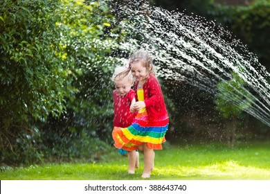 Child Playing With Garden Sprinkler. Preschooler Kid Running And Jumping. Summer Outdoor Water Fun In The Backyard. Children Play With Hose Watering Flowers. Kids Run And Splash On Hot Sunny Day.