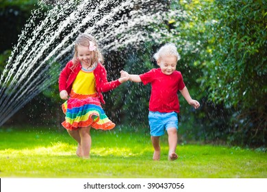 Child Playing With Garden Sprinkler. Preschooler Kid Run And Jump. Summer Outdoor Water Fun In The Backyard. Children Play With Hose Watering Flowers. Kids Splash On Sunny Day. Selective Focus On Boy.