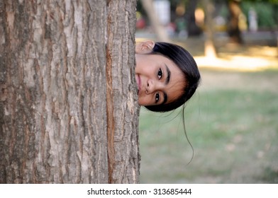 Child playing hide and seek. Cute little girl hiding behind huge tree.