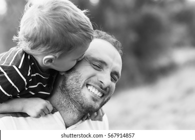 Child Playing With His Father. Child Kissing Father. Daddy Playing Active Games With His Son Outside. Happy Family Portrait. Laughing Dad With Little Boy Enjoying Together. Black And White Photo.