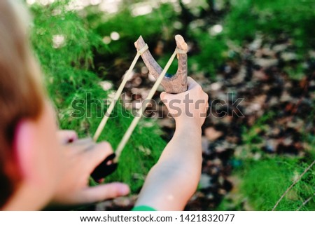 Child playing with his slingshot in a park having fun in freedom.