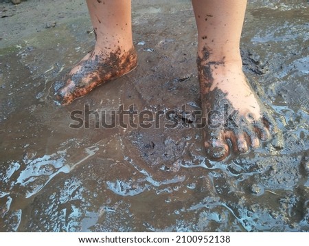A child playing in the mud gets his feet and hands dirty