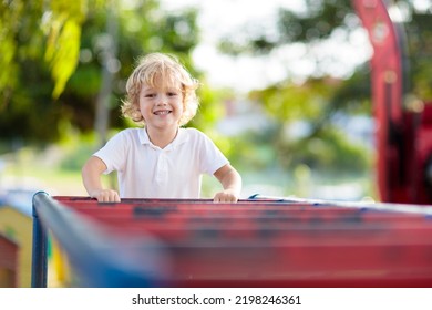 Child Playing On Outdoor Playground In Rain. Kids Play On School Or Kindergarten Yard. Active Kid On Colorful Monkey Bars. Healthy Summer Activity For Children. Little Boy Climbing.