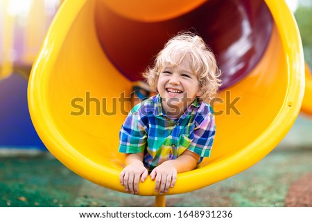 Child playing on outdoor playground. Kids play on school or kindergarten yard. Active kid on colorful slide and swing. Healthy summer activity for children. Little boy climbing outdoors.