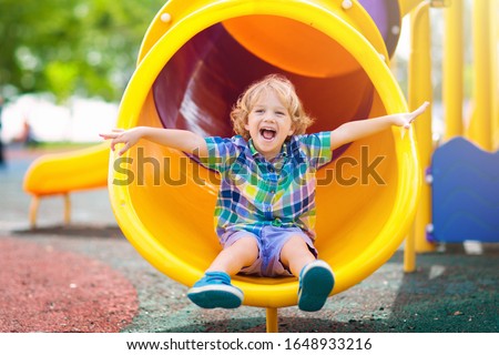 Child playing on outdoor playground. Kids play on school or kindergarten yard. Active kid on colorful slide and swing. Healthy summer activity for children. Little boy climbing outdoors.