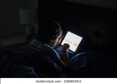 Child Playing On A Tablet In Bed