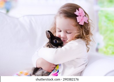 Child Playing With A Real Rabbit. Kids Play With Pets. Little Girl Holding Bunny. Children And Animals At Home Or Preschool. Cute Curly Toddler Kid Hugs Her Pet Animal. Preschooler Feeding Rabbits.