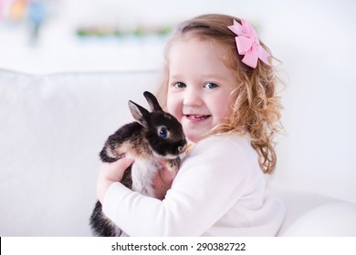 Child Playing With A Real Rabbit. Kids Play With Pets. Little Girl Holding Bunny. Children And Animals At Home Or Preschool. Cute Curly Toddler Kid Hugs Her Pet Animal. Preschooler Feeding Rabbits.