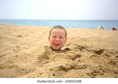 A child is playing in the sand, the child's head is visible from the sand on the beach