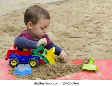 Child Playing In Sandpit With Toy Truck Car Or Digger.