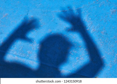 Child Playing Scary Prank With Its Own Shadow On A Blue Iron Background.