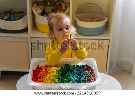Child playing with sensory bin with dried pasta in rainbow colors. Dyed pasta for play and craft activities. Montessori material. Sensory play and learning colors activity for kids. 