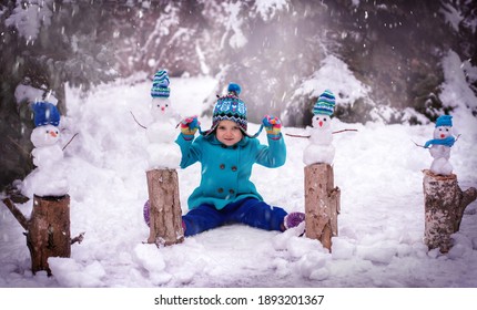 child playing in snow. Little girl in a blue coat and four little snowmen on a snowy background. Copy space. Winter fun.