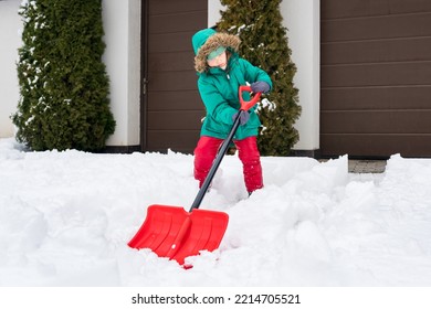 Child Playing In  Snow With Shovel. Girl Shoveling Fresh Snow And Clearing Sidewalks Near Home After Snowstorm. Kids Removaling Snow After Heavy Snowfall