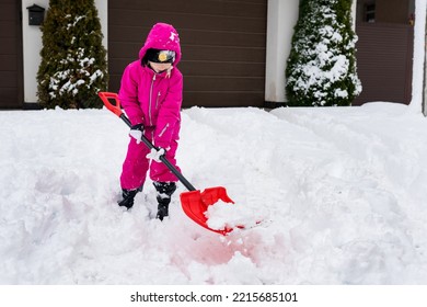 Child Playing In Snow With Shovel. Girl Shoveling Fresh Snow And Clearing Sidewalks Near Home After Snowstorm. Kids Removaling Snow After Heavy Snowfall