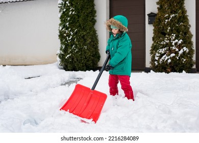 Child Playing In Snow With Shovel. Girl Shoveling Fresh Snow And Clearing Sidewalks Near Home After Snowstorm. Kids Removaling Snow After Heavy Snowfall