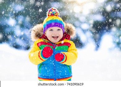 Child playing with snow in winter. Little boy in colorful jacket and knitted hat catching snowflakes in winter park on Christmas. Kids play and jump in snowy forest. Children catch snow flakes