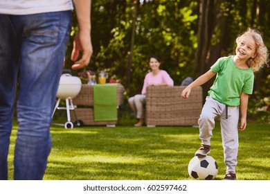 Child playing soccer ball with father in garden